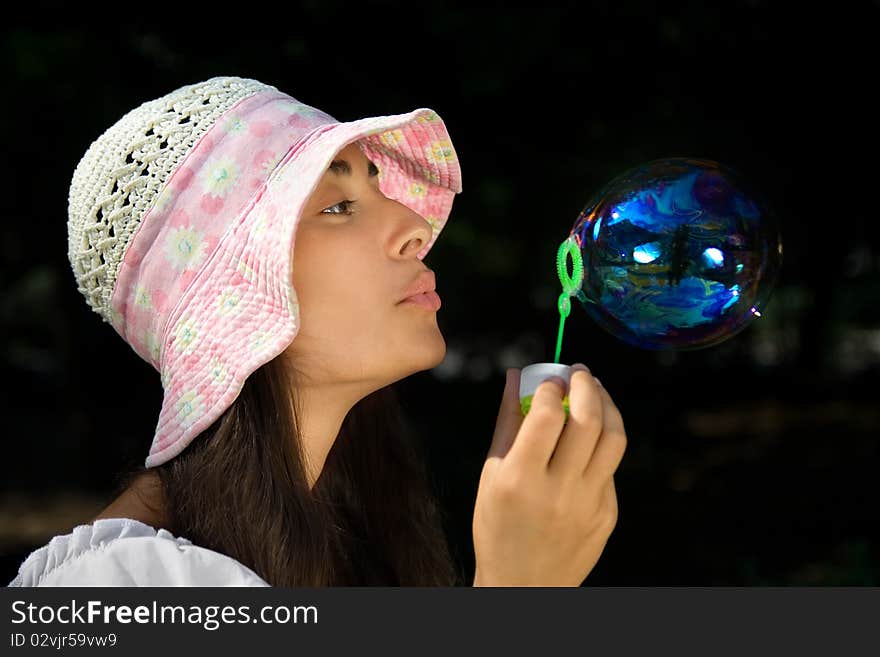 Young girl in the bonnet blowing bubbles outdoors