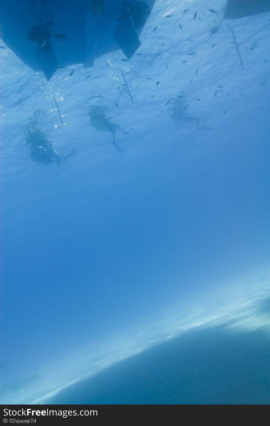 Underwater view of three scuba diver silhouettes at the back of their dive boat. Temple, Sharm el Sheikh, Red Sea, Egypt. Underwater view of three scuba diver silhouettes at the back of their dive boat. Temple, Sharm el Sheikh, Red Sea, Egypt.