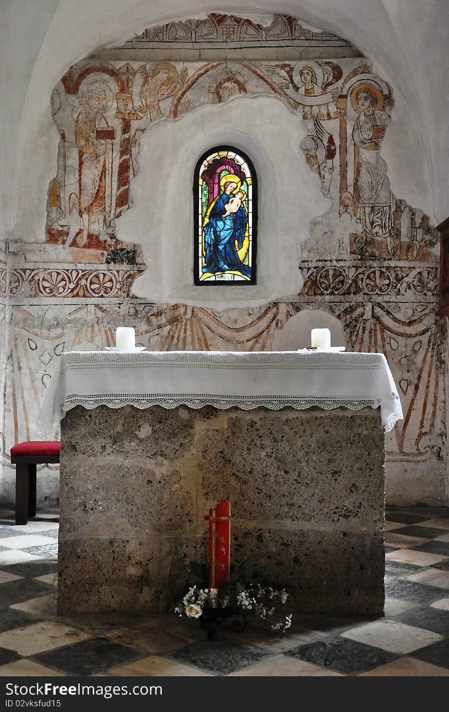 Image shows interior of a church with altar, two candles and a coloured window. Image shows interior of a church with altar, two candles and a coloured window.