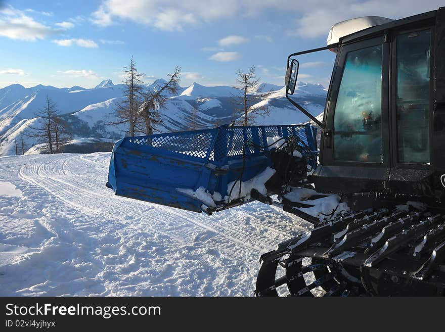 A part of black snowcat with cabin. Caterpillar track on the snow. Evening mountains background. A part of black snowcat with cabin. Caterpillar track on the snow. Evening mountains background