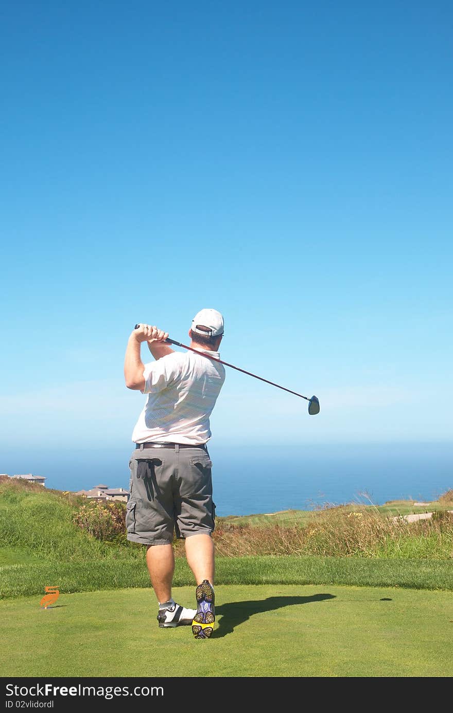 Young male golfer hitting the ball from the tee box next to the ocean on a beautiful summer day. Young male golfer hitting the ball from the tee box next to the ocean on a beautiful summer day