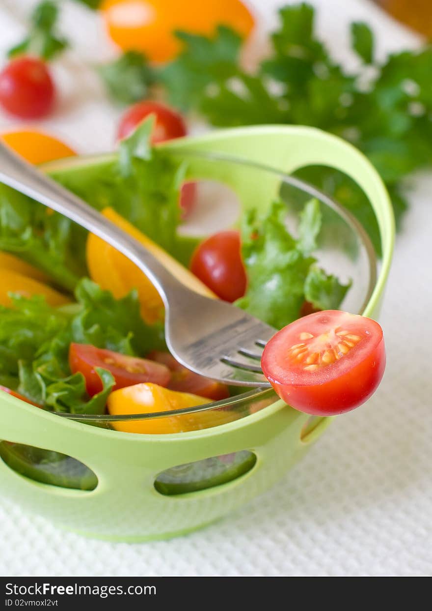 A fresh ripe tomato on a fork with bowl of salad on backround. A fresh ripe tomato on a fork with bowl of salad on backround