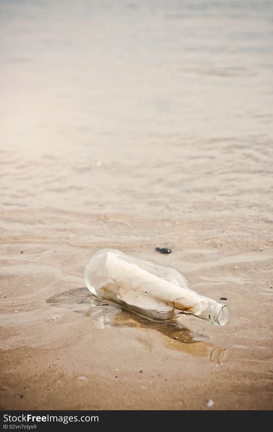 A glass bottle in water on a sandy beach. A glass bottle in water on a sandy beach