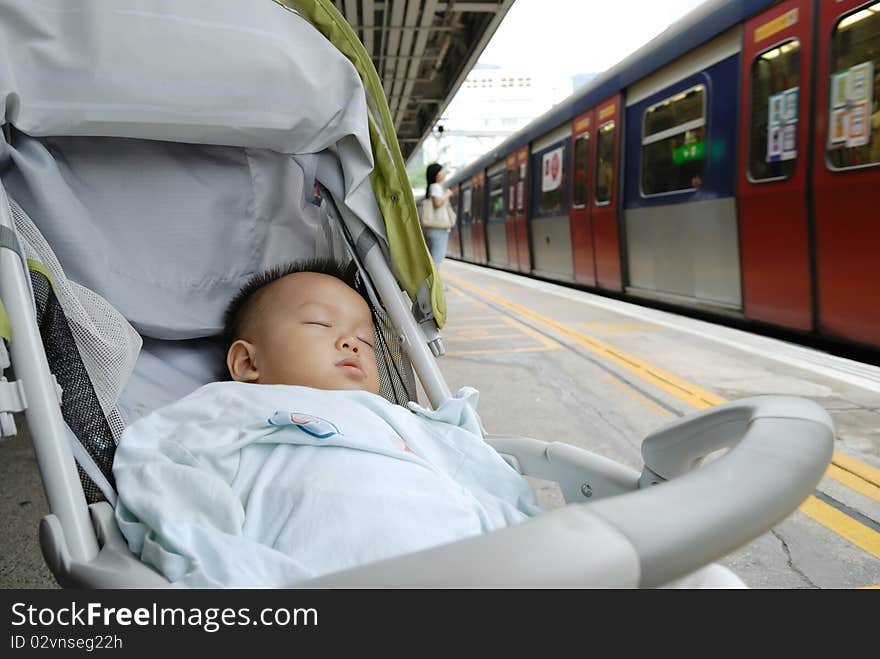 In the platform, a chinese boy is sleeping in the baby carrier when waiting the train. In the platform, a chinese boy is sleeping in the baby carrier when waiting the train.