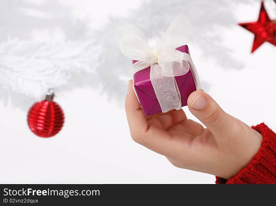 Hand holding a christmas gift with a white christmas tree in the background