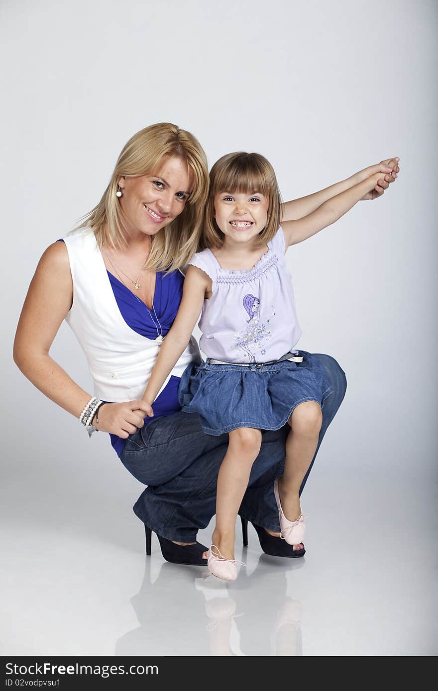 Full length portrait of two, young pretty mother and cute little daughter, smiling, studio image. Full length portrait of two, young pretty mother and cute little daughter, smiling, studio image