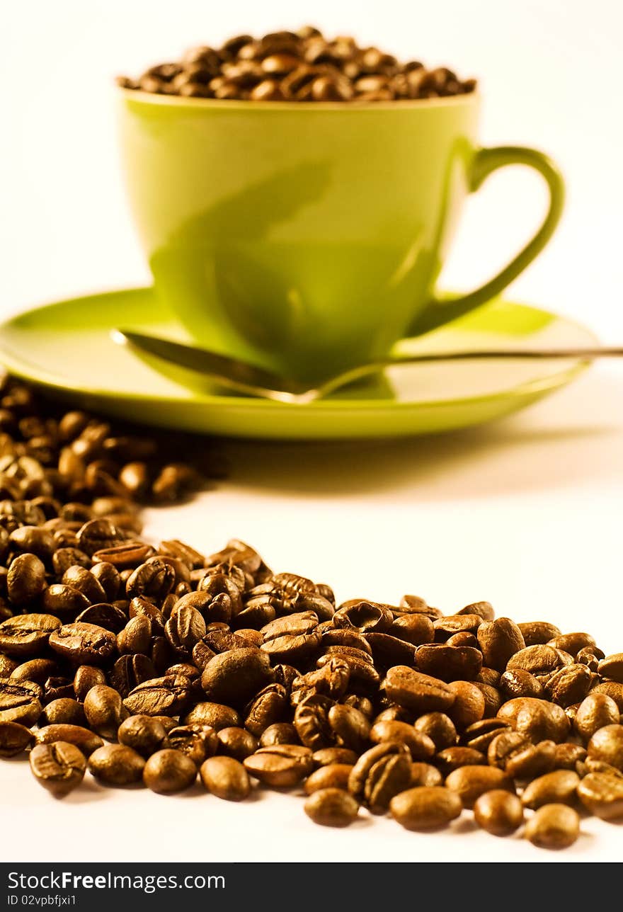 Green cup of coffee with brown beans on white ground