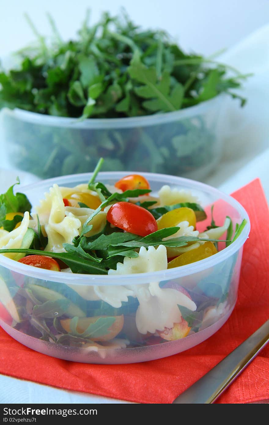 Salad with tomatoes and arugula and pasta in a glass bowl