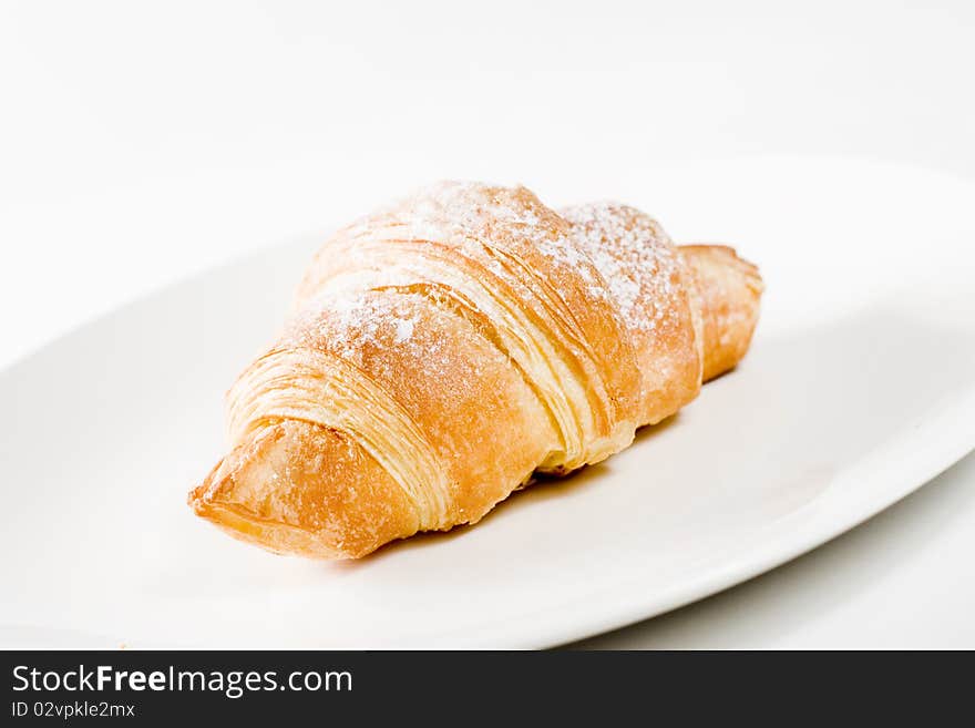 Fresh croissant on white plate with powdered sugar