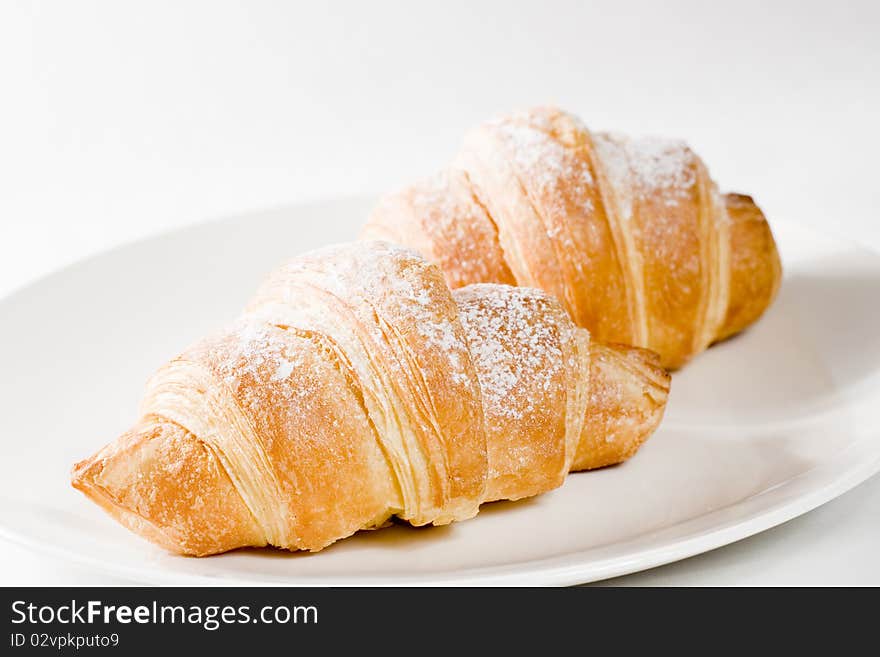 Fresh croissants on white plate with powdered sugar .