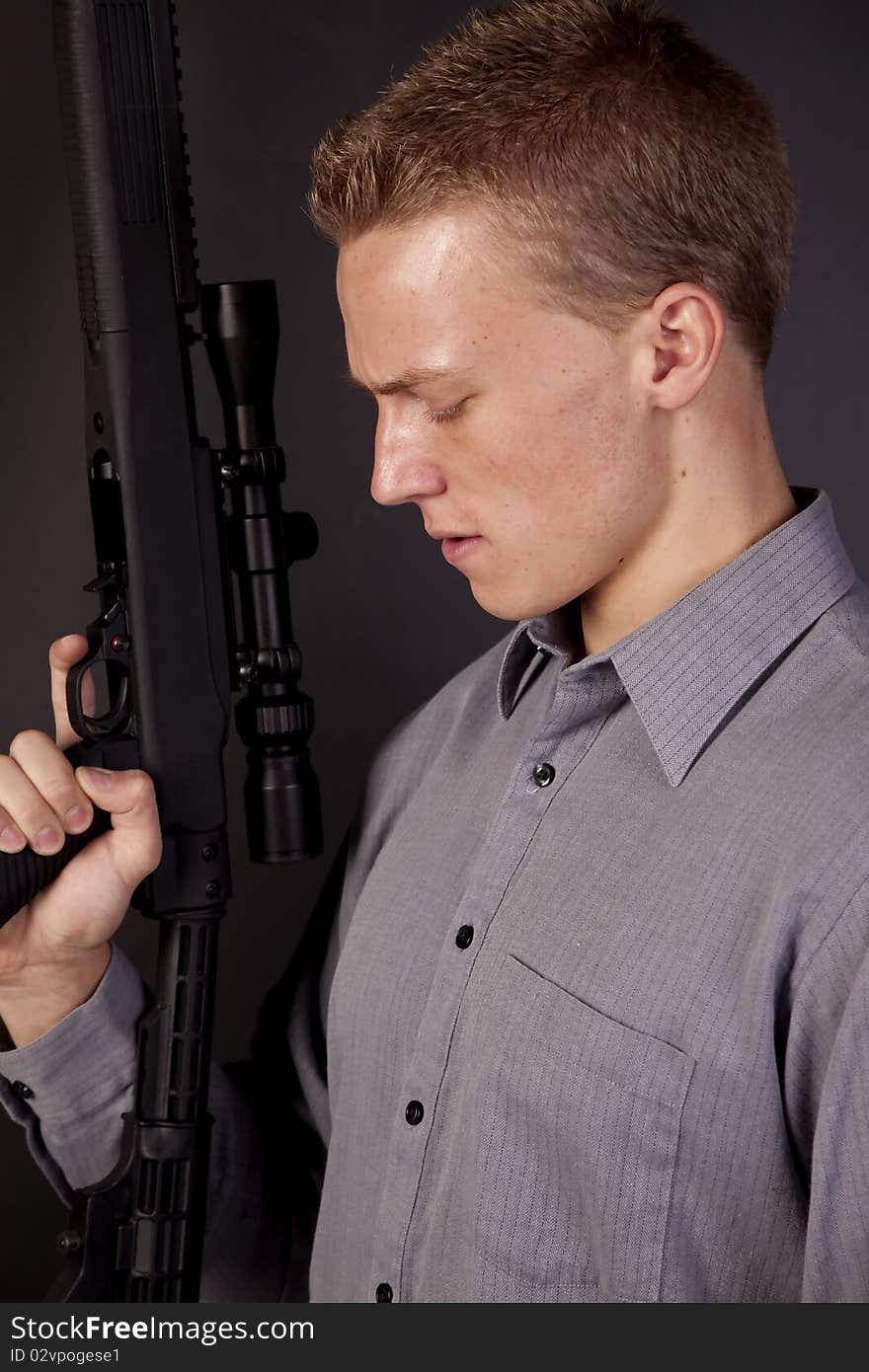 A young man holding a gun looking down at the trigger. A young man holding a gun looking down at the trigger.