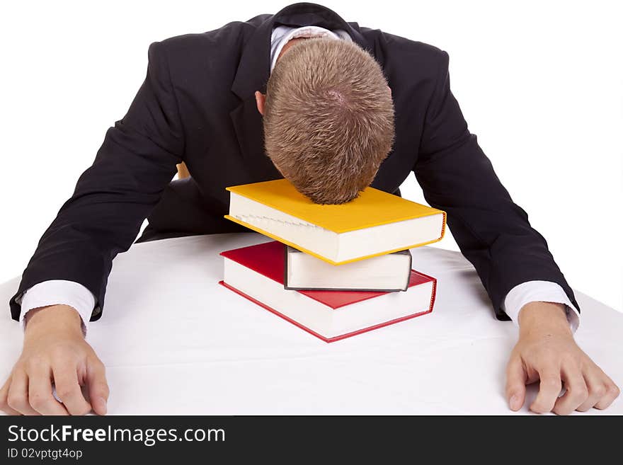 A young business man sitting at a table with his head on a stack of books giving up. A young business man sitting at a table with his head on a stack of books giving up.