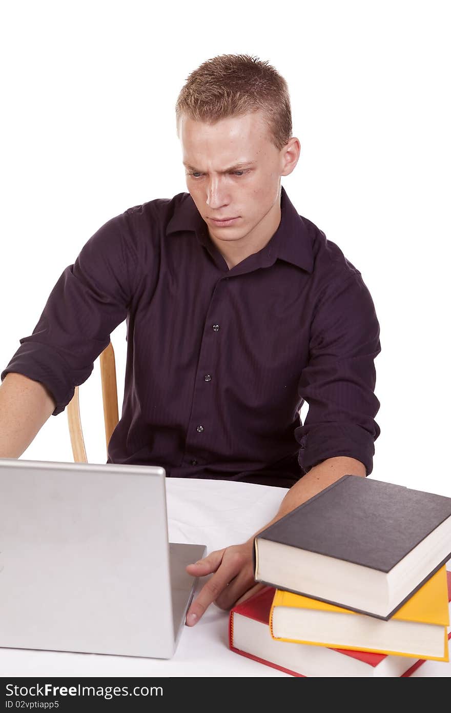 A young man sitting and working on his laptop with a stack of books. A young man sitting and working on his laptop with a stack of books.