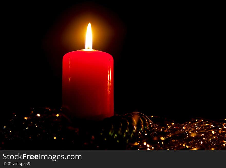 Burning candle with a glass toy in a tinsel on a black background. Burning candle with a glass toy in a tinsel on a black background