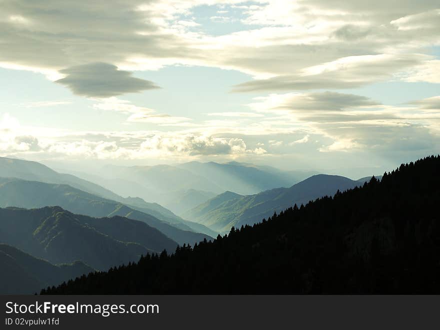 Mountain peeks and dark forest with a blue cloudy sky. Mountain peeks and dark forest with a blue cloudy sky