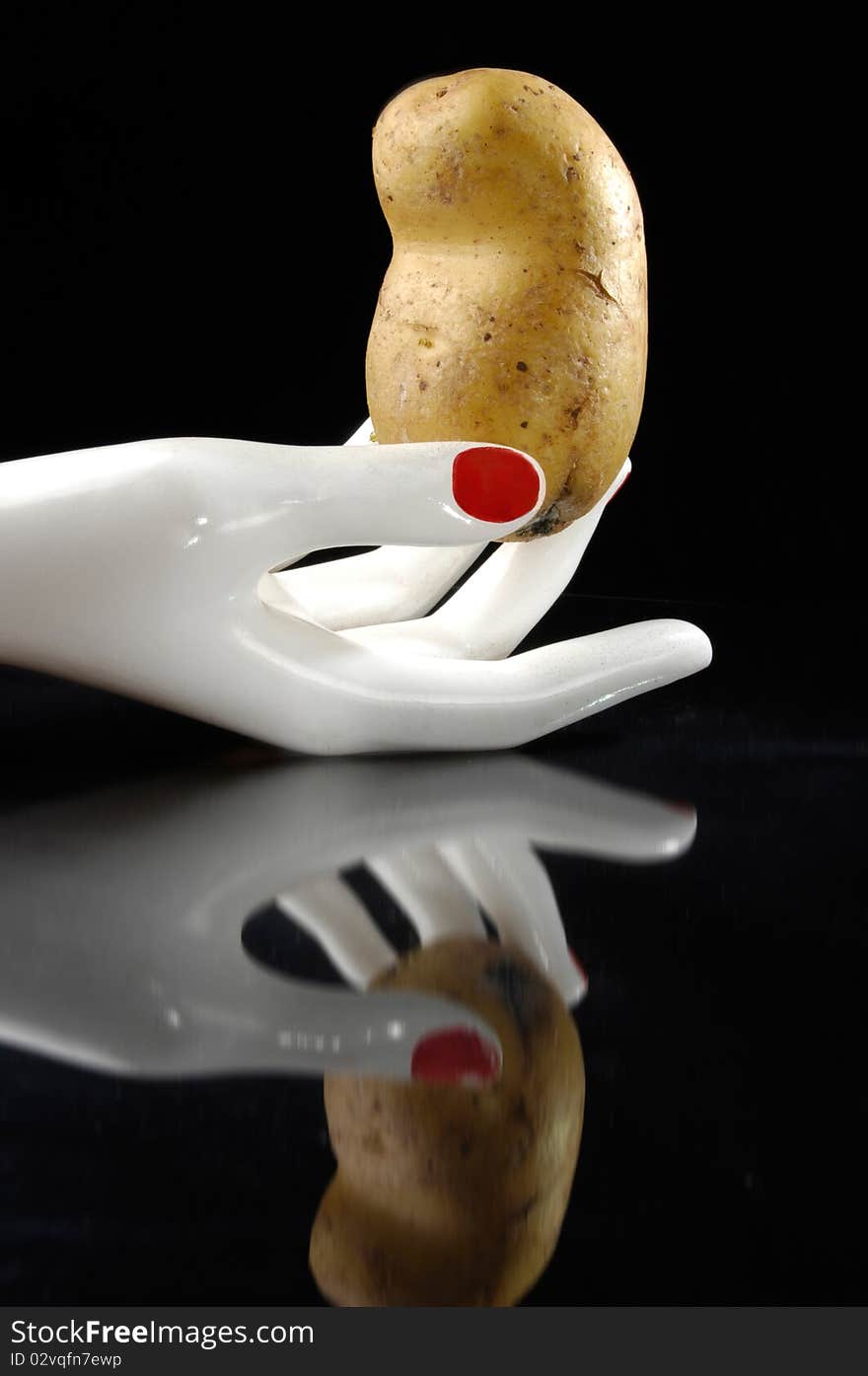 Potato in the white hand with reflection. Black background. Potato in the white hand with reflection. Black background