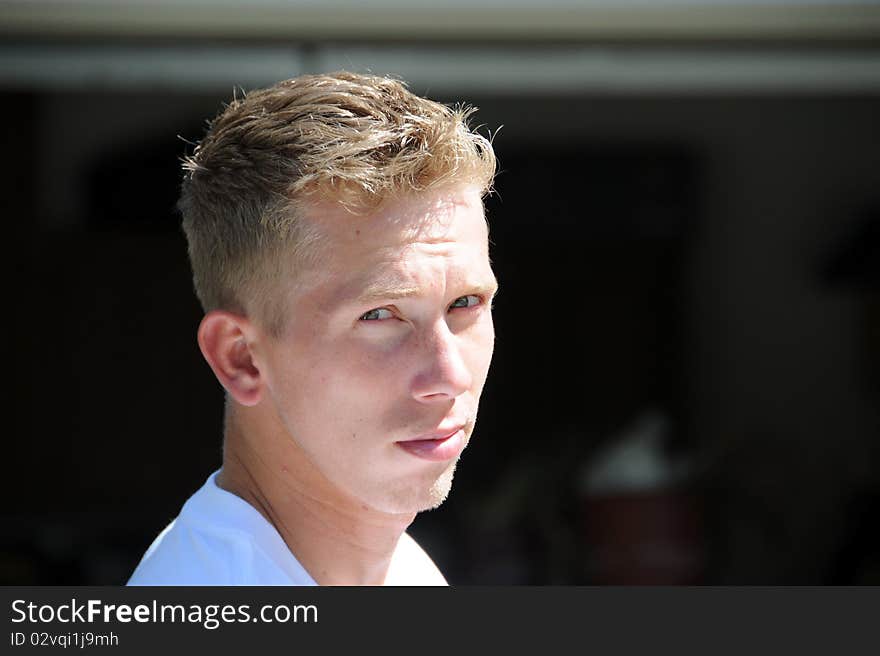 An adult male is standing outside on a summer day, he has a serious and thoughtful look on his face.