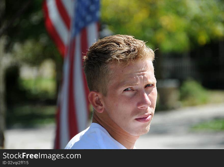 An adult male is standing outside on a summer day, he has a serious and thoughtful look on his face.