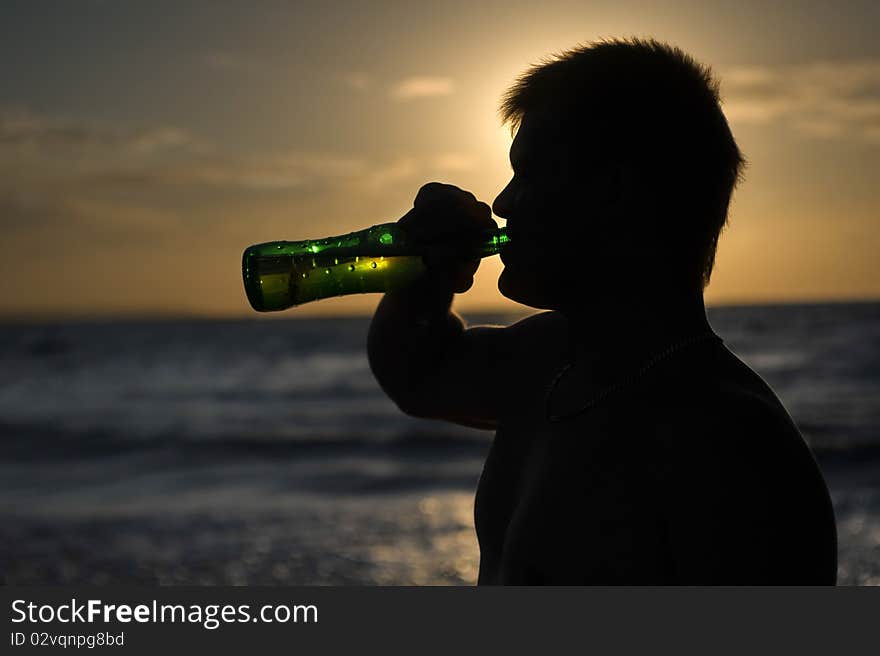 Silhouette of a man drinking beer on the on the beach