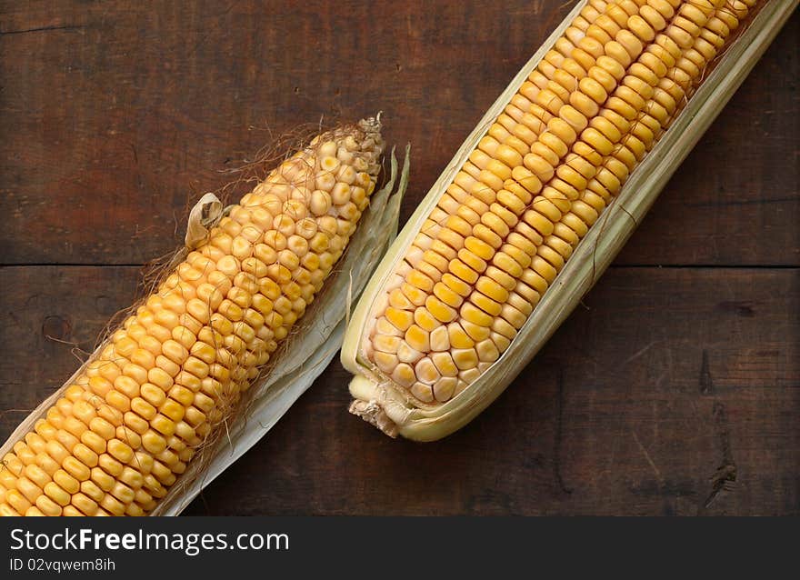 Two raw corncobs lying on wooden background. Two raw corncobs lying on wooden background