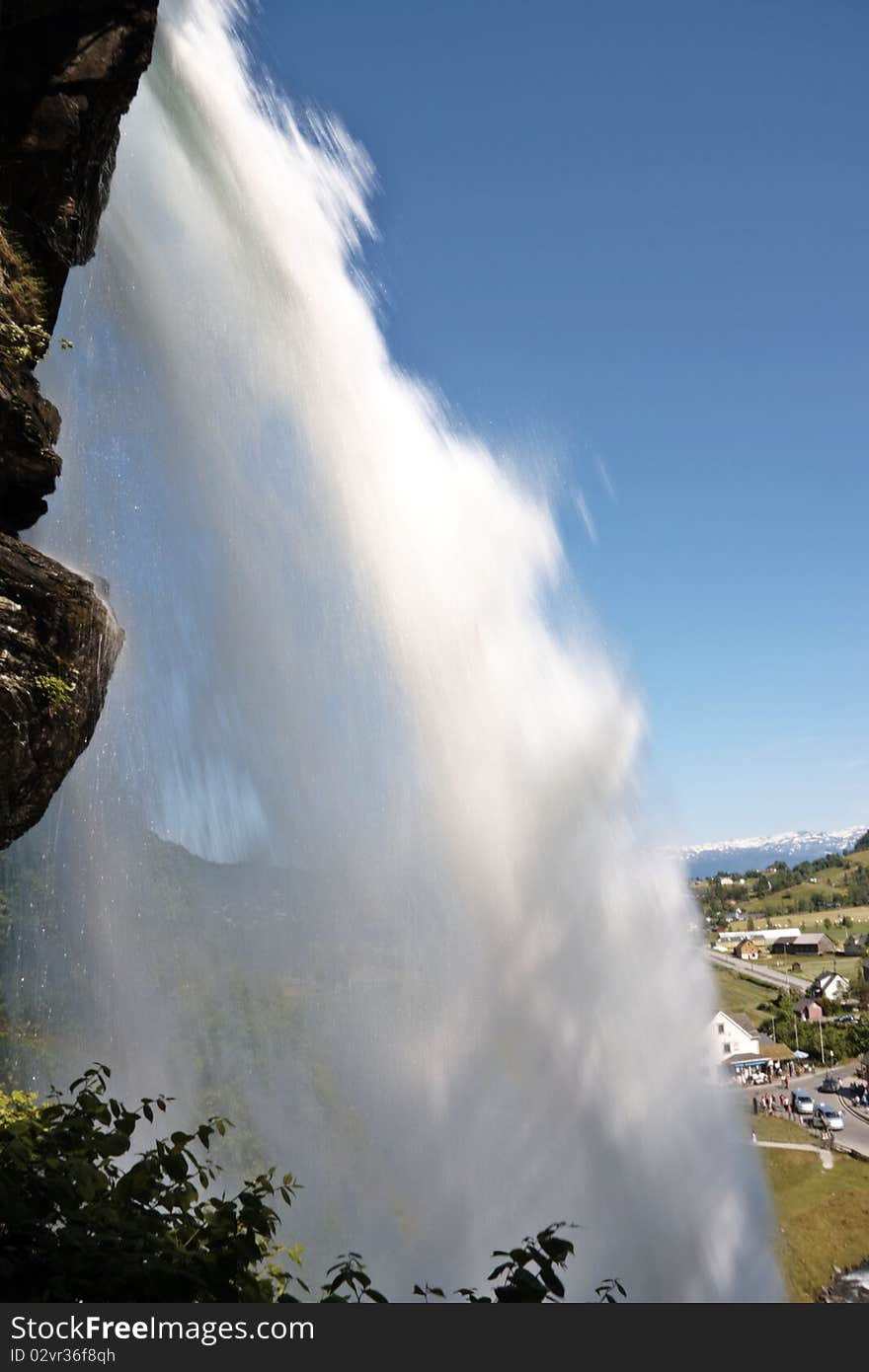 View behind a waterfall with green field as a background