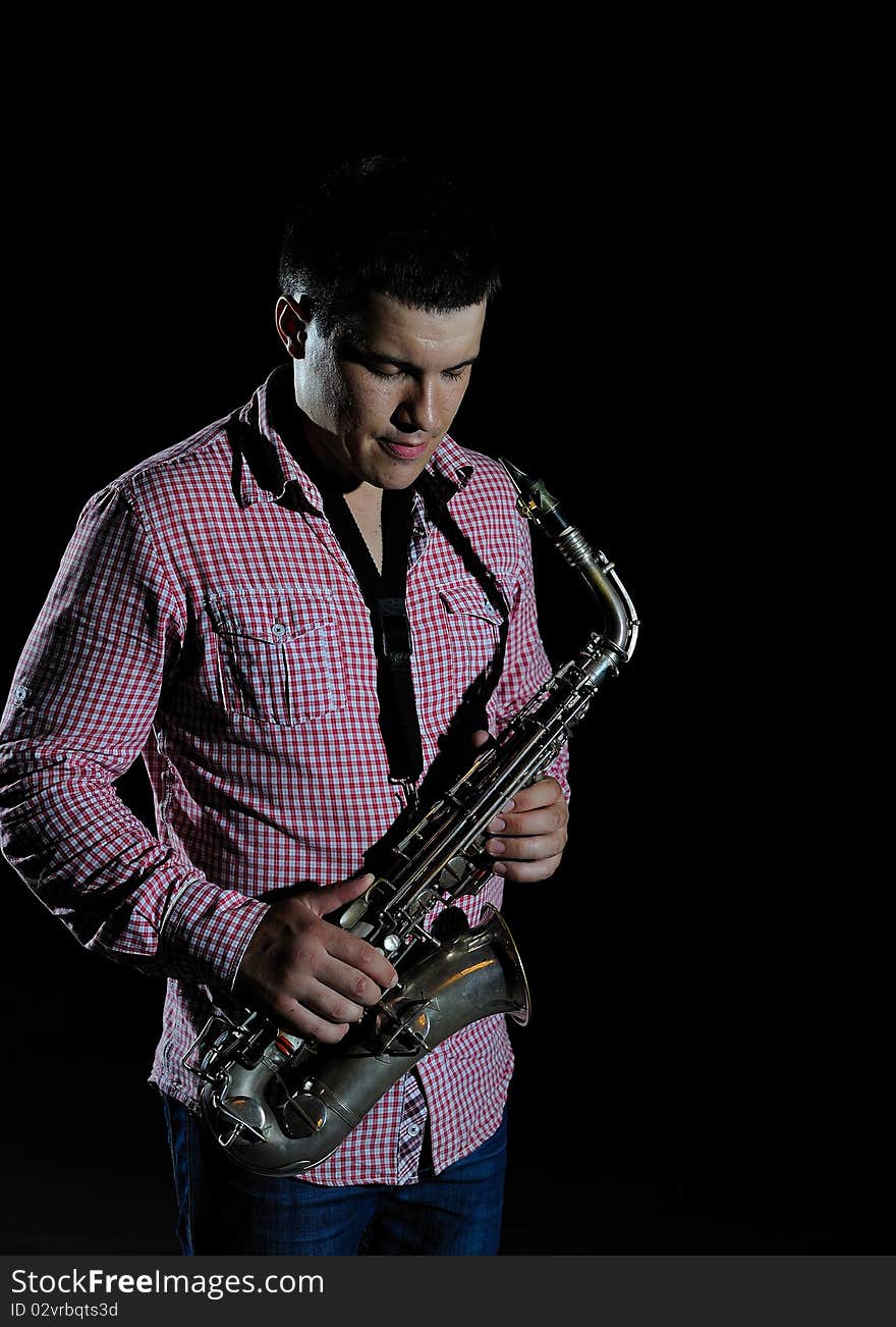 Young handsome man playing music on saxophone. black background