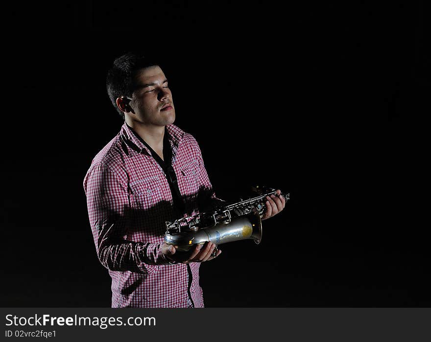 Young handsome man playing music on saxophone. black background