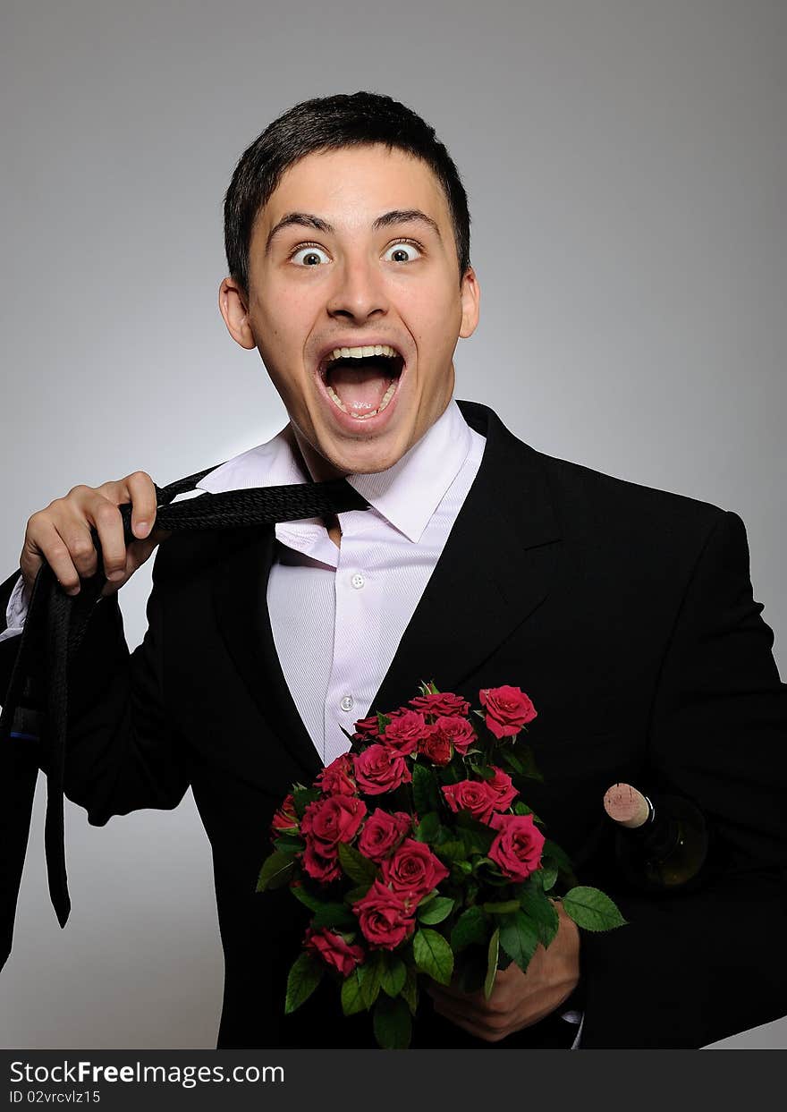 Handsome romantic young man holding rose flower and vine bottle prepared for a date. gray background