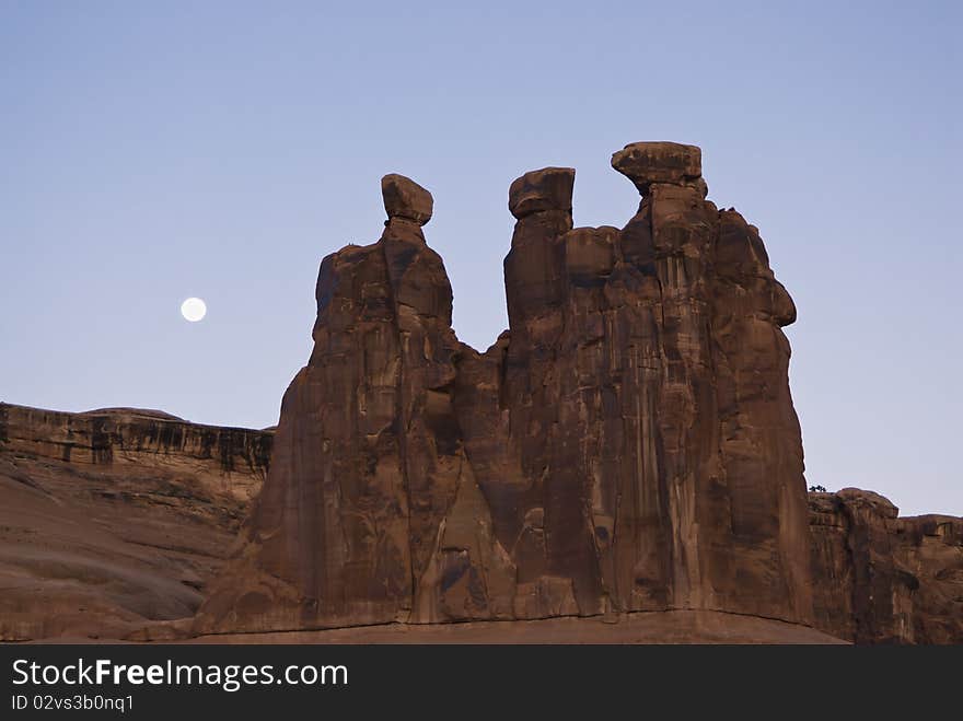 A full moon sets behind the Three Gossips formation in Arches National Park.