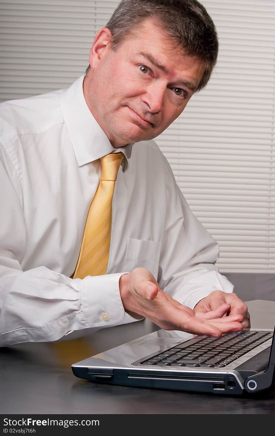 Businessman gestures to laptop and looks at camera with smile. Businessman gestures to laptop and looks at camera with smile.