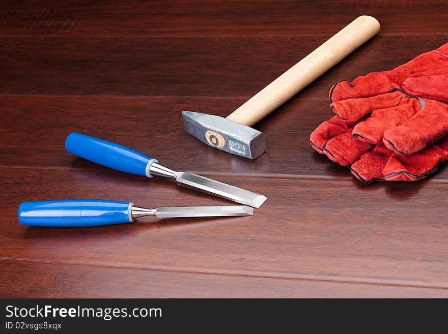 Red gloves, hammer and blue chisels on dark background. Red gloves, hammer and blue chisels on dark background