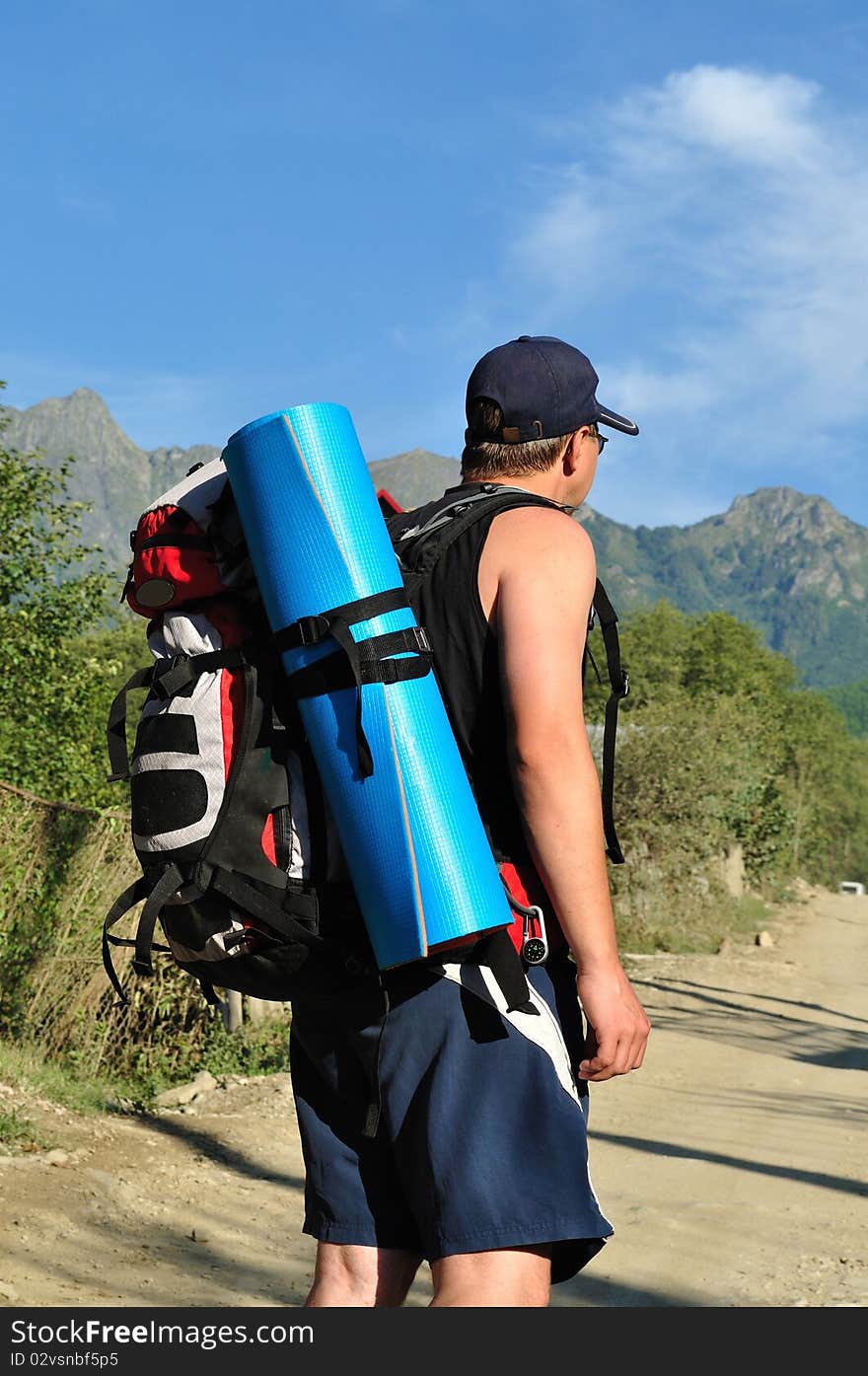 Tourist with a large backpack is a high mountain, on the road, photo from the back