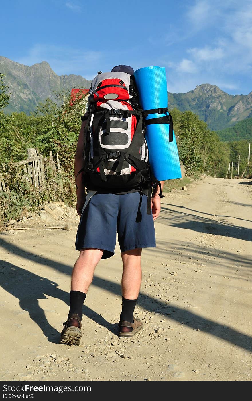 Tourist with a large backpack is a high mountain, on the road, photo from the back