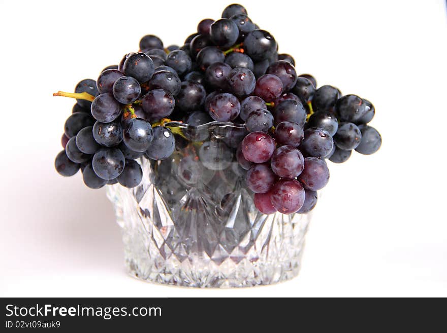 Black grapes in a crystal vase on a white background