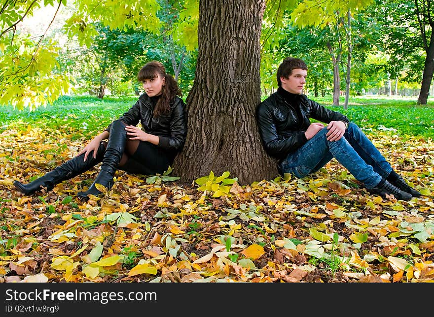 The enamoured sit on leaves in autumn park. The enamoured sit on leaves in autumn park