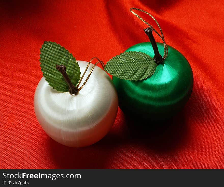 Two apple decorations on a red silk background. Two apple decorations on a red silk background