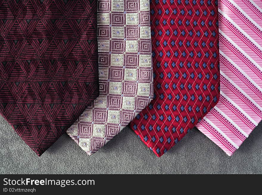 Four ties in red, pink, burgundy and white tones, with assorted designs, on a gray background. Four ties in red, pink, burgundy and white tones, with assorted designs, on a gray background.