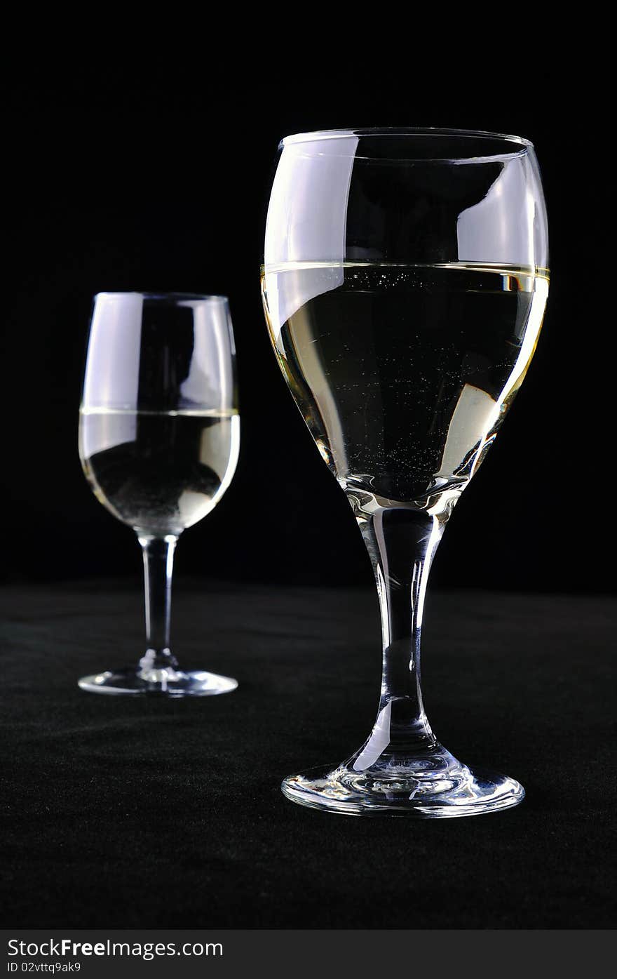 Two glasses of white wine, separated from each other, on a black background