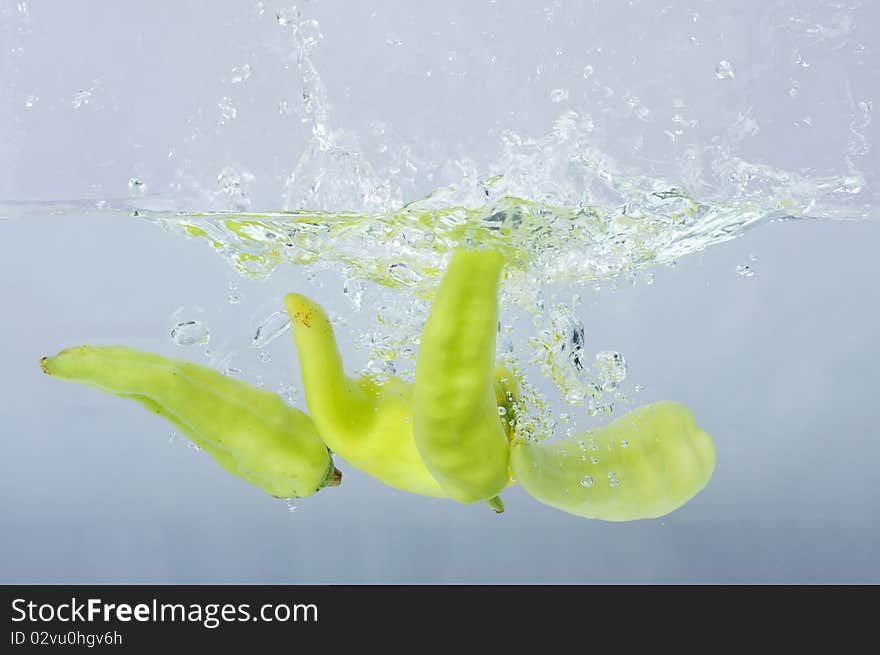 Green chilli thrown in water with gray background