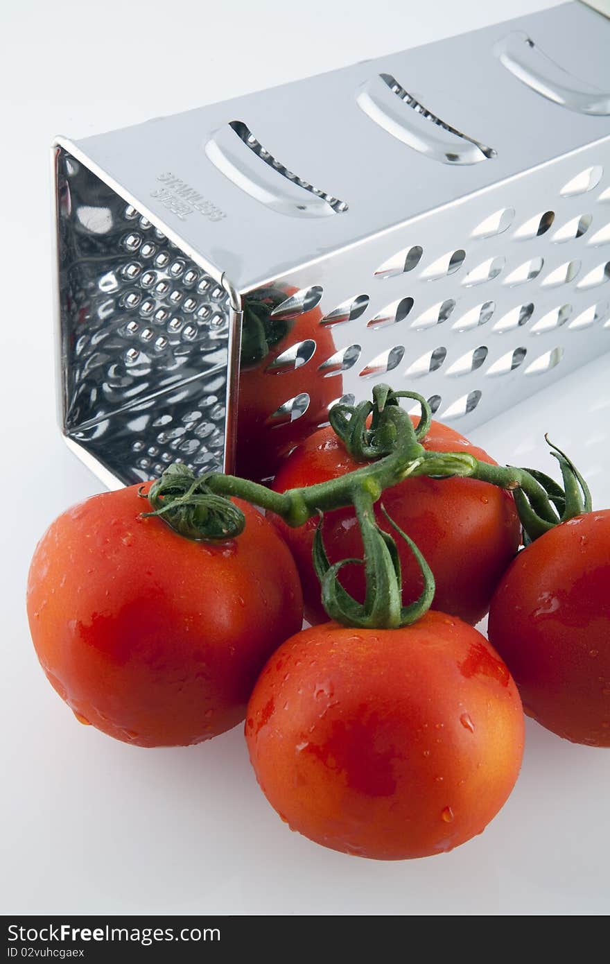 Red tomatoes and grater on white background