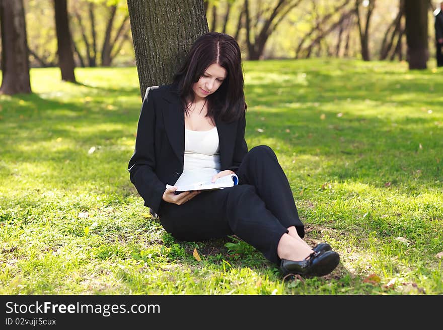 Young businesswoman sitting on the grass and reading book outdoor. Young businesswoman sitting on the grass and reading book outdoor