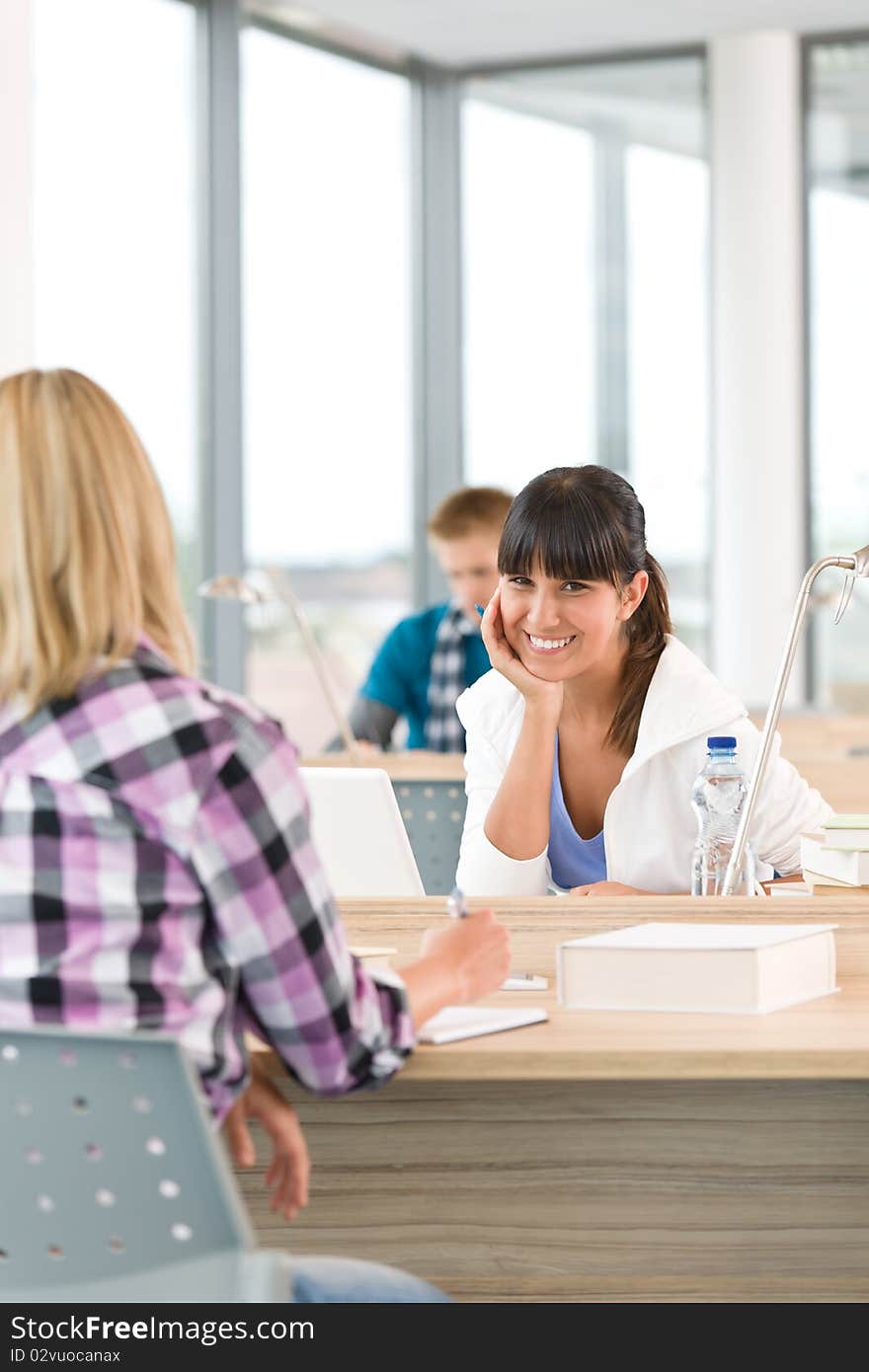 Three high school students in classroom studying with books and laptop