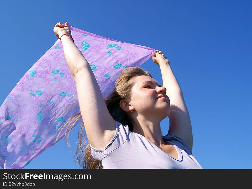 The woman holds in hands over a head a female scarf against the dark blue sky. The woman holds in hands over a head a female scarf against the dark blue sky