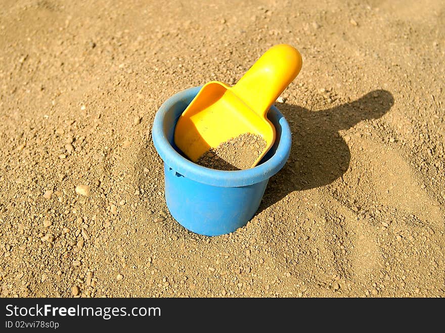 The children's yellow scoop lays in a bucket with sand. The children's yellow scoop lays in a bucket with sand