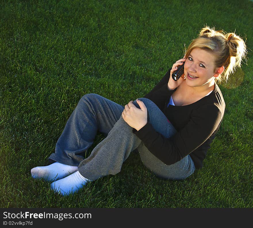 Beautiful young teenage girl sitting on the grass talking on the phone. Beautiful young teenage girl sitting on the grass talking on the phone