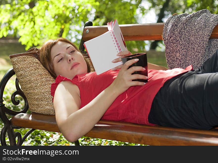 Woman laying on bench with coffee and reading. Woman laying on bench with coffee and reading