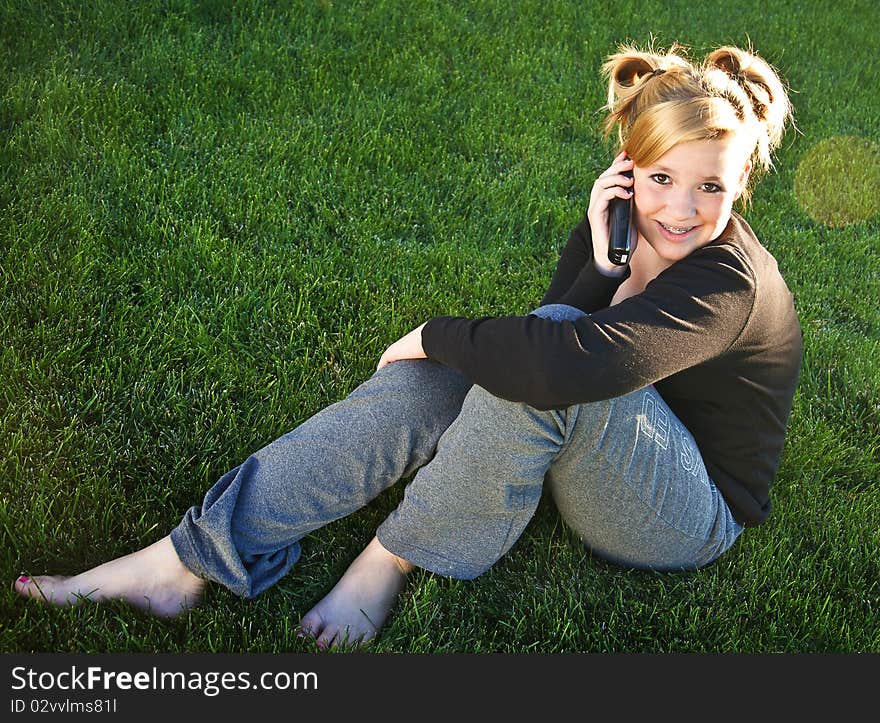 Beautiful young teenage girl sitting on the grass talking on the phone. Beautiful young teenage girl sitting on the grass talking on the phone