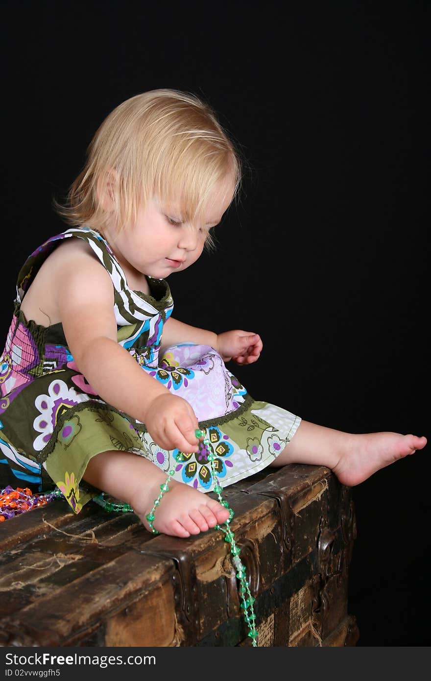 Beautiful blond toddler sitting on an antique trunk playing with beads. Beautiful blond toddler sitting on an antique trunk playing with beads