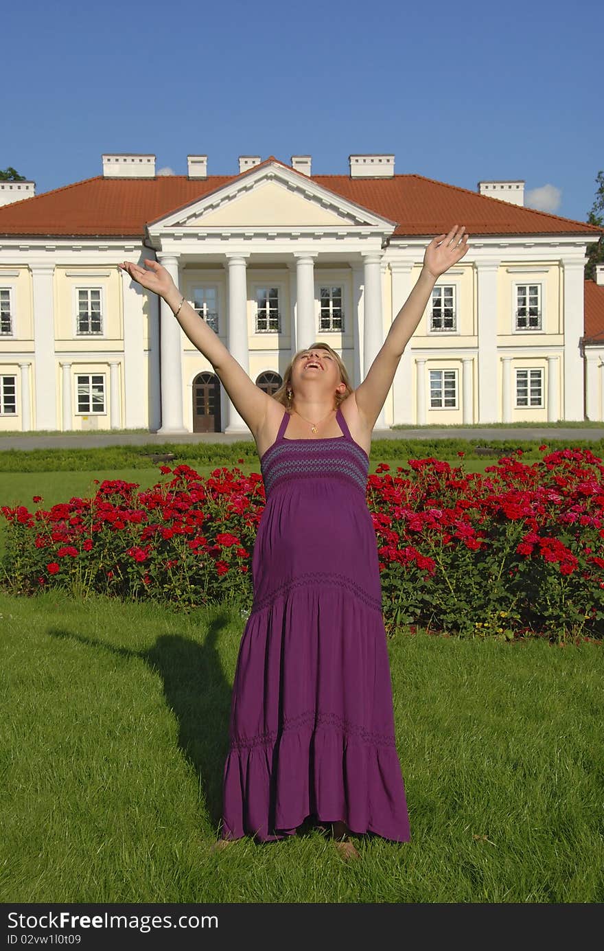 Happy pregnant woman in the garden in front of the palace