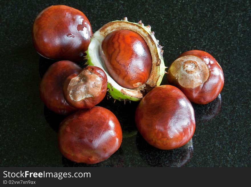 A collection of gleaming conkers against a black granite background